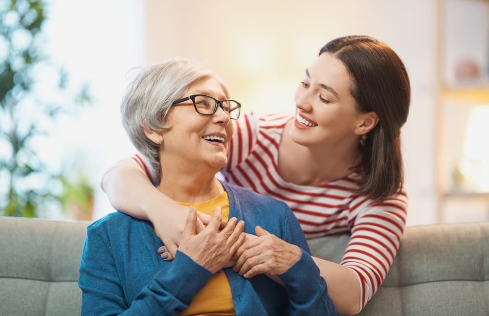 A smiling older woman and a younger woman embrace warmly, showcasing healthy, happy smiles that highlight the importance of quality orthodontic care for all ages – Denver Orthodontics.