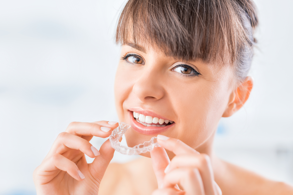 Woman Inserting Clear Aligner With a Bright Smile – Invisalign in Cherry Creek A woman gently places a clear aligner onto her teeth while smiling, emphasizing the ease, comfort, and near-invisibility of aligner-based orthodontics – Invisalign in Cherry Creek.