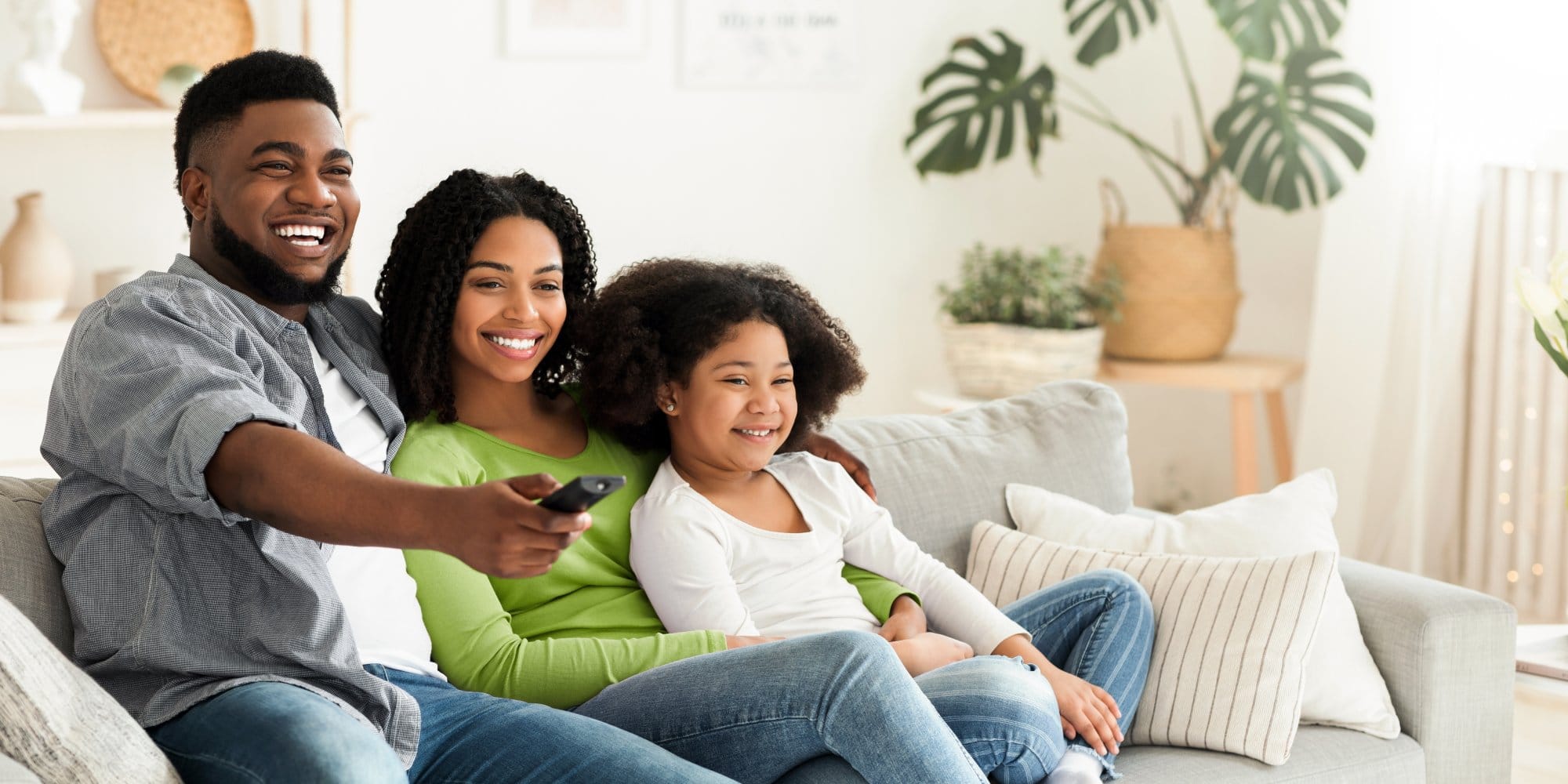 Smiling african american family relaxing and watching tv in living room, staying at home during quarantine, happy father switching channels