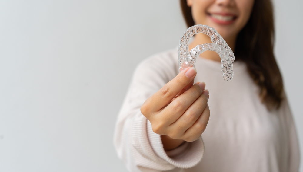 Woman Holding Upper and Lower Clear Aligners – Invisalign in Cherry Creek A smiling woman presents both upper and lower clear aligner trays, demonstrating the precision and effectiveness of advanced orthodontic treatment – Invisalign in Cherry Creek.