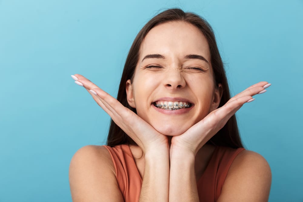A joyful young woman poses with a bright smile and visible metal braces, reflecting confidence and excitement throughout her orthodontic journey – Braces in Highland.