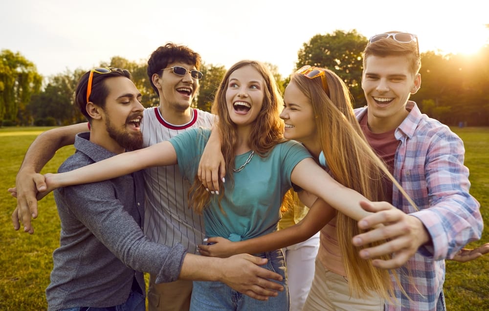 A joyful group of young friends share a big laugh together in a sunny park, showing off bright, healthy smiles that reflect confidence and happiness – Orthodontist in Lakewood CO.