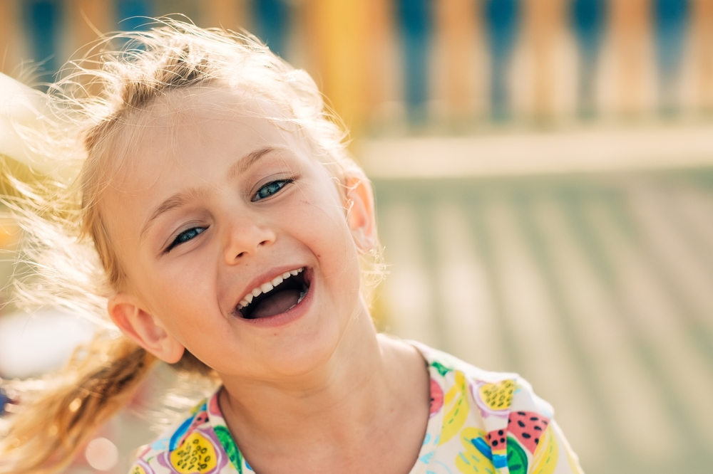 A happy child laughing in the sunlight, showcasing the importance of early orthodontic evaluation for healthy teeth alignment - Phase 1 Orthodontics