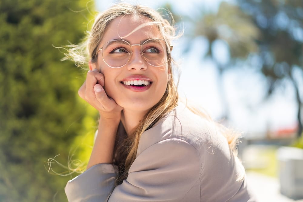A young woman with glasses smiles joyfully in the sunshine, showcasing a bright and healthy smile that reflects exceptional orthodontic care – Highlands Ranch Orthodontics.